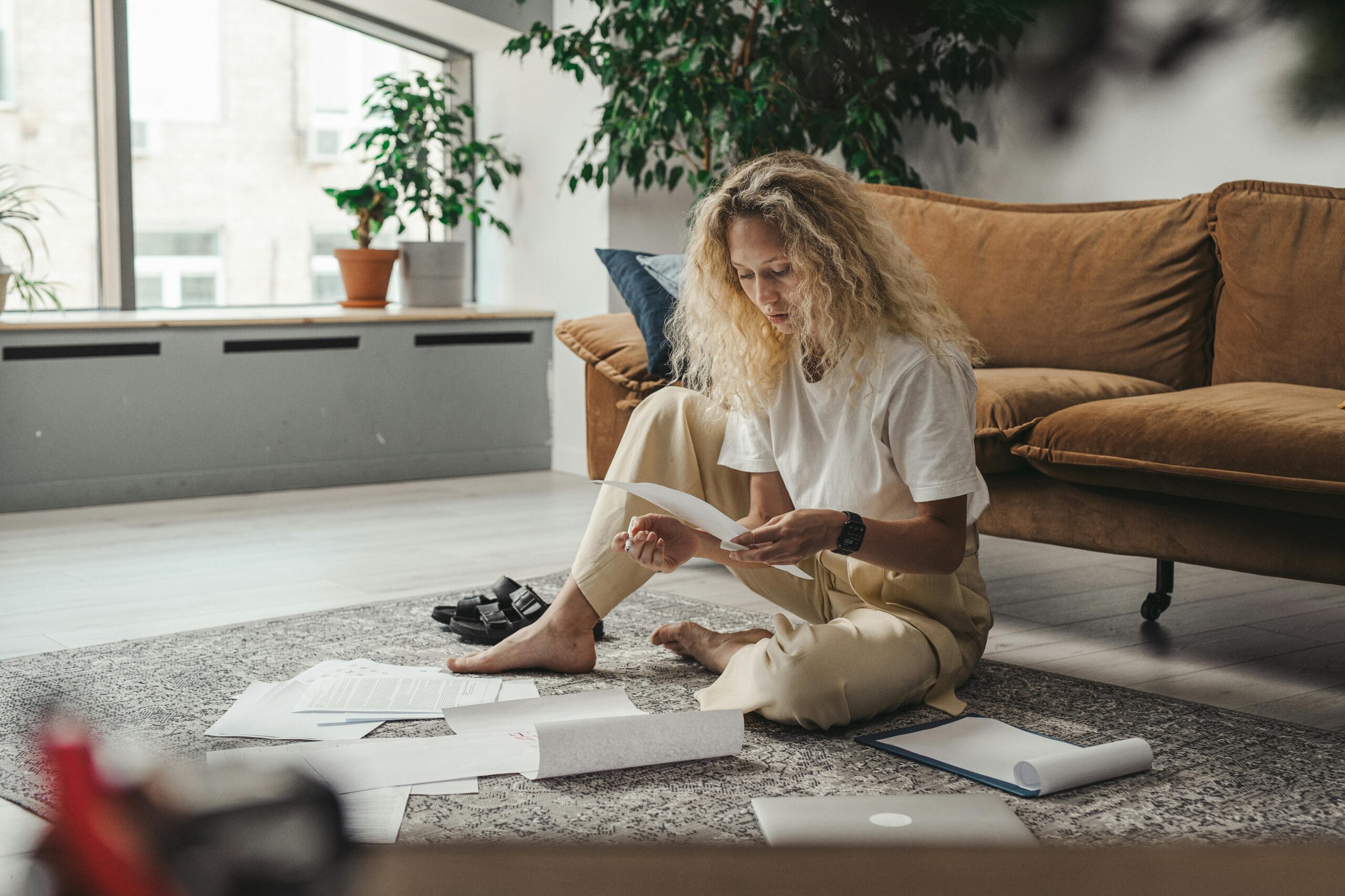 Woman sitting on the floor at home, reviewing paperwork in a relaxed environment.